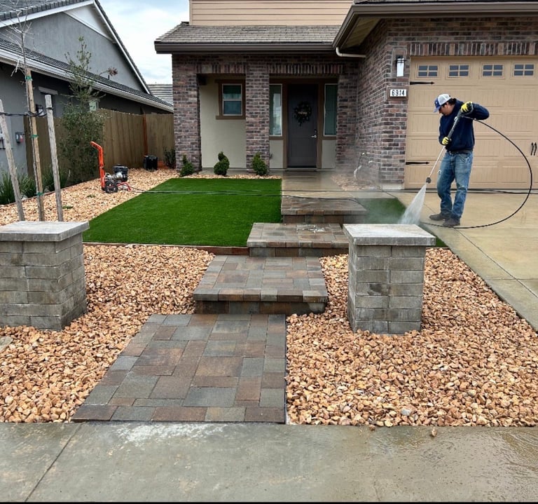 Worker power washing front entrance of brick home with stone pathway and landscaping