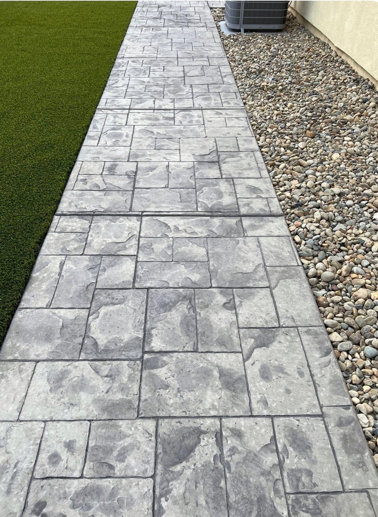 Gray stone paver pathway bordered by green lawn on left and gravel on right, leading toward house